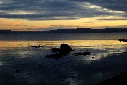 A bird sitting on a joint boulder rock on a colourful evening