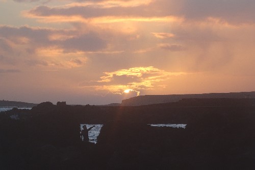 A silhouette lady seen pointing at the sunset the sunset in between some large boulders