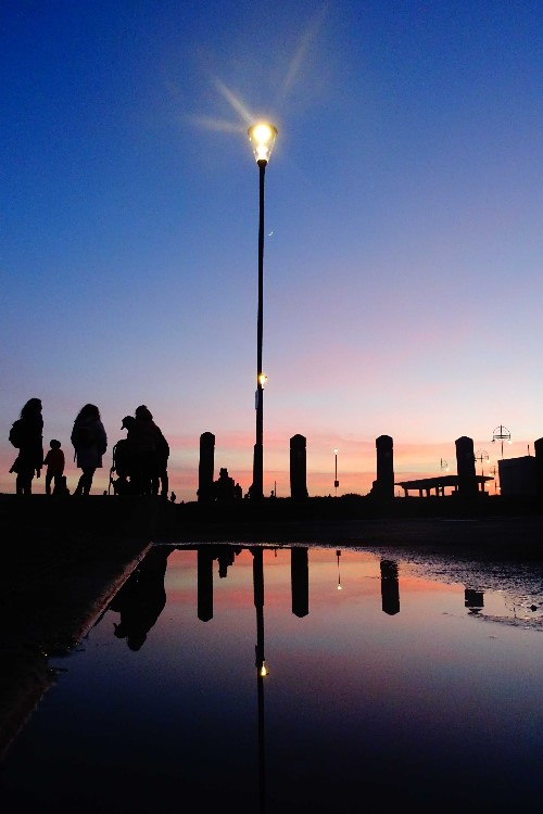 Refelctions from a puddle as people enjoy the night sky colours together
