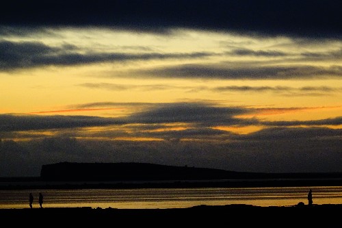 A dark mystical scene of people walking at the tail end of sunset