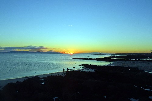 Two people calmly having a chat at the edge of the Atlantic ocean, with dramatic sunset in the backdrop